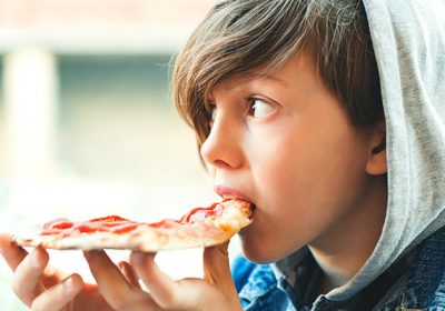 Pilkonowa Strefa Gastronomiczna. Fotografia młodego chłopca jedzącego pizzę na świeżym powietrzu.